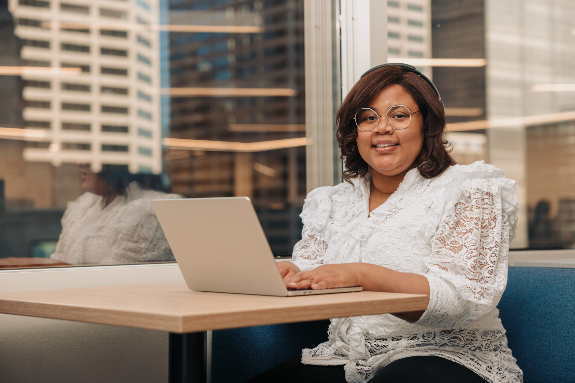 A young woman with a developmental disability works on a laptop in an office. Behind her, a window reveals a cityscape.