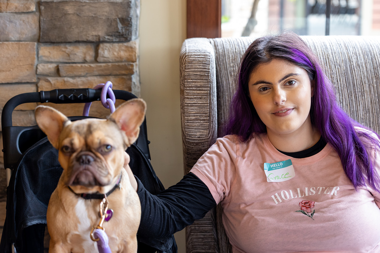 Teenage girl with purple hair sits in a chair petting her dog, while at the Marin Self Determination Resource Fair.