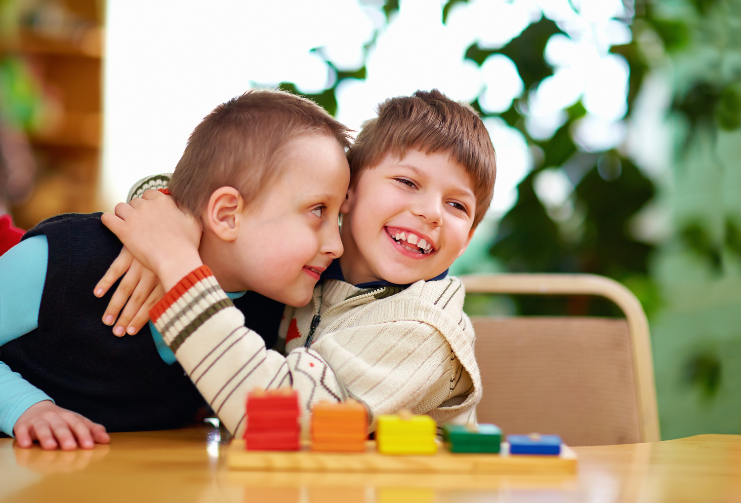 Two disabled boys hugging happily in bright, sunny preschool.