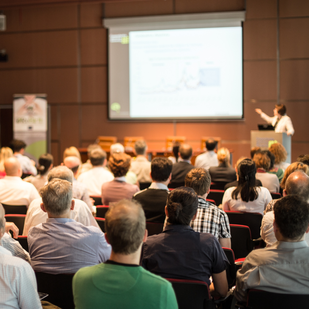 Speaker presenting to an audience in a full conference room.