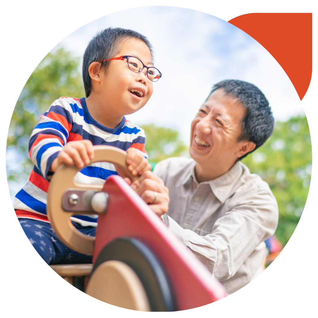 Asian boy with down syndrome is enjoying time with his father outdoors at a public park on a sunny day.