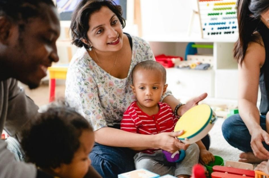 Mother sitting with her son in a group preschool setting, holding a tambourine.