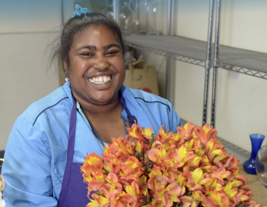 Person with I/DD smiles while holding a bouquet of orange flowers they put together.
