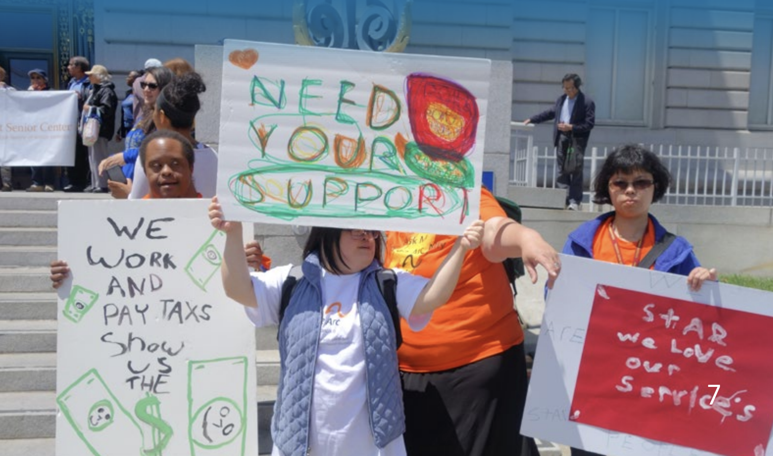 Four people with disabilities standing outside a California legislative building holding colorful signs.