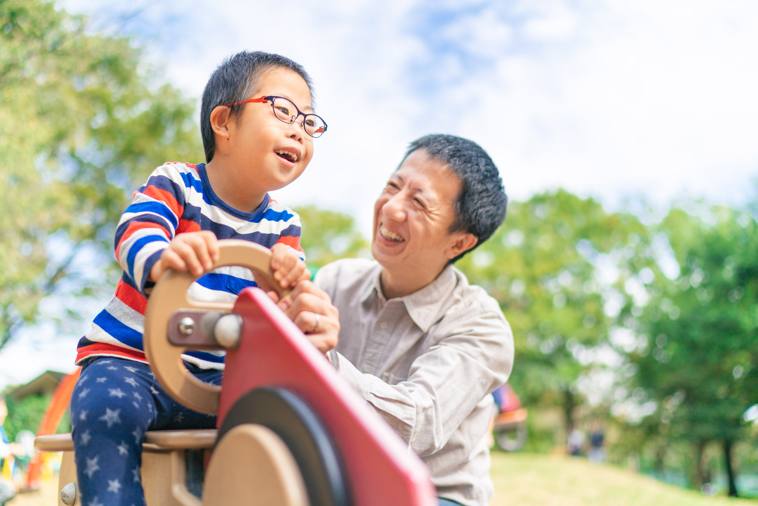Asian boy with down syndrome is enjoying time with his father outdoors at a public park on a sunny day.