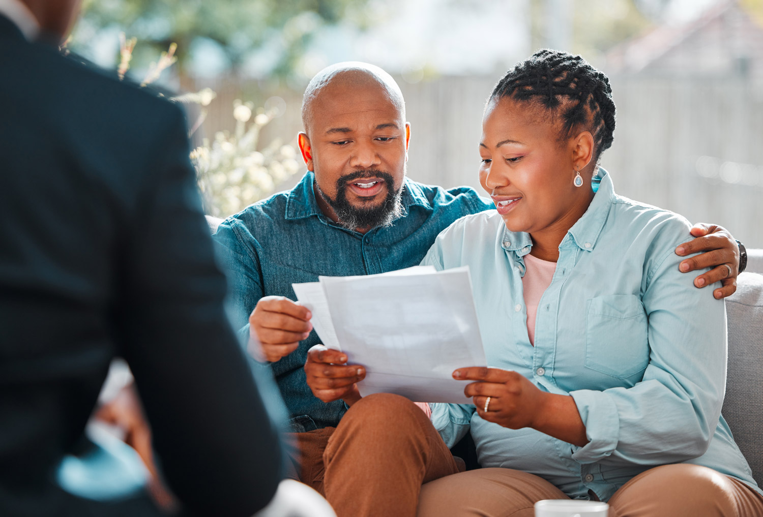 Two black parents sitting on a couch reading a report and smiling.