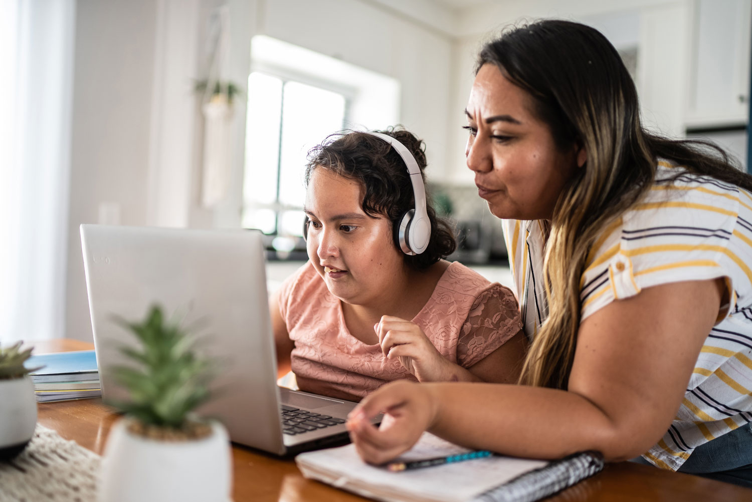 Mother helping her daughter with a psychomotor intellectual disability use their laptop while studying at home.