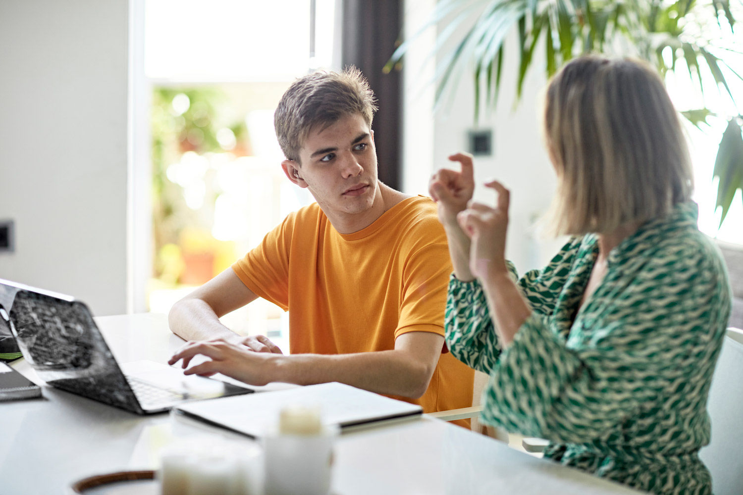 Deaf mother signing with son while they work together on a laptop.