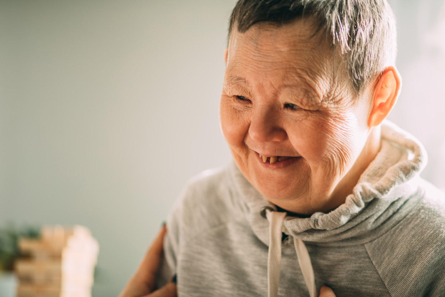 An elderly woman with Down syndrome, accompanied by an assistant who supports her, holds her hands.