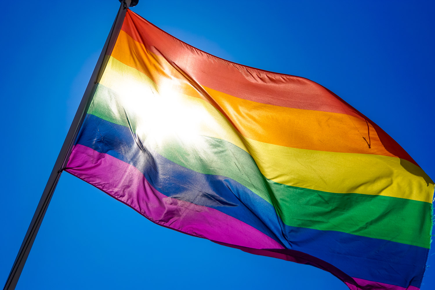 Rainbow flag representing LGBTQIA+ community waving in the wind on a sunny, clear day.