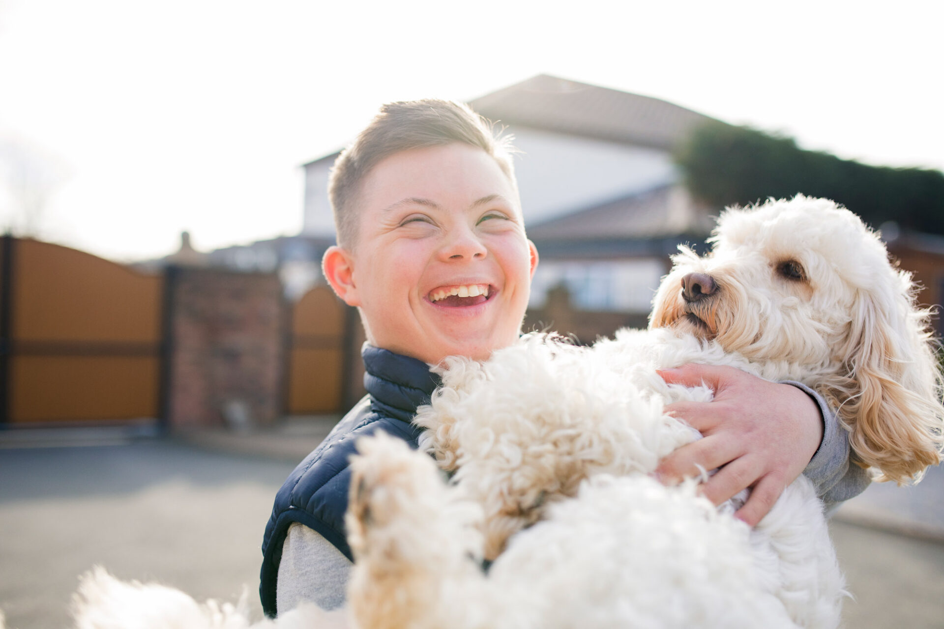 A boy with down syndrome hugs his pet dog in the driveway.